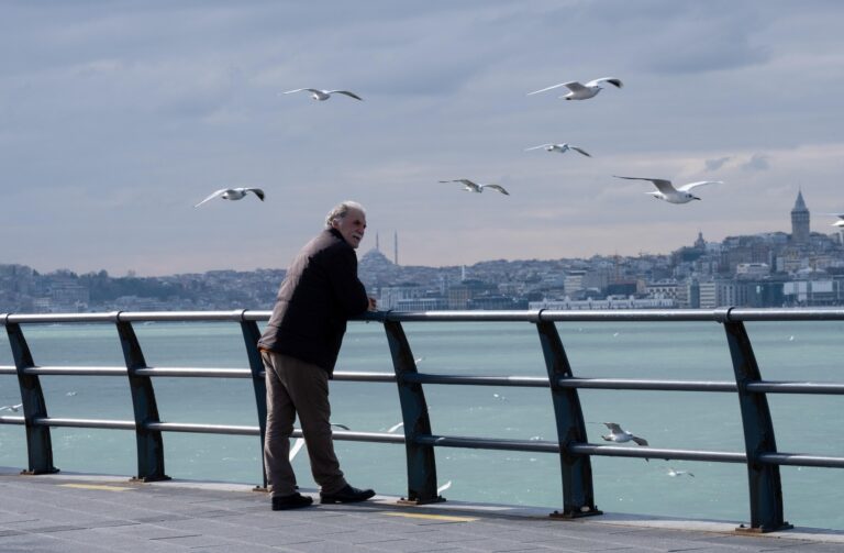 An elderly professional taking a peaceful lunch break on a city bridge, looking out over the urban skyline with a calm and content expression.